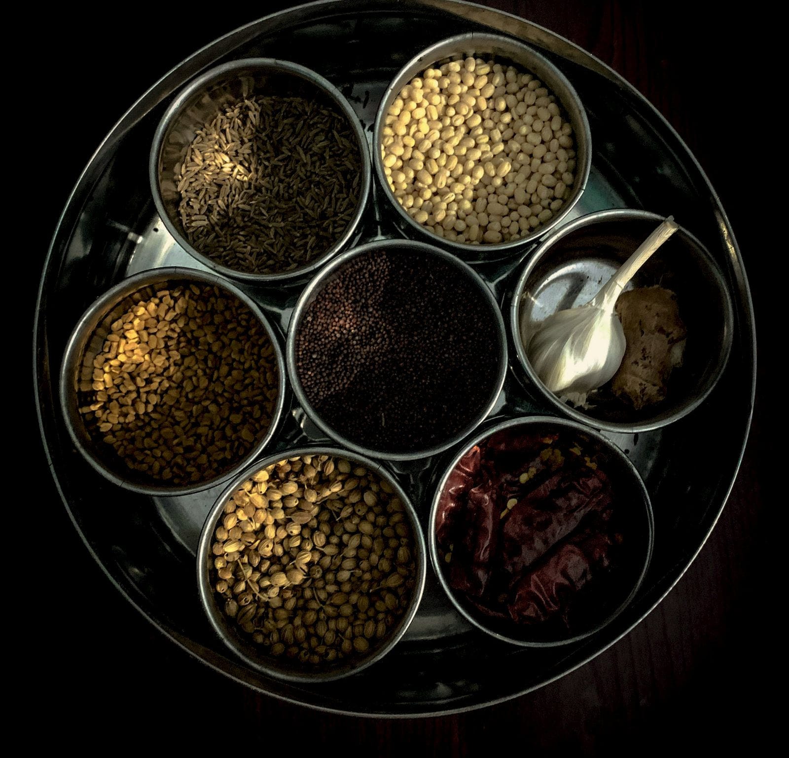 A steel spice box with seven measured compartments, seen from above