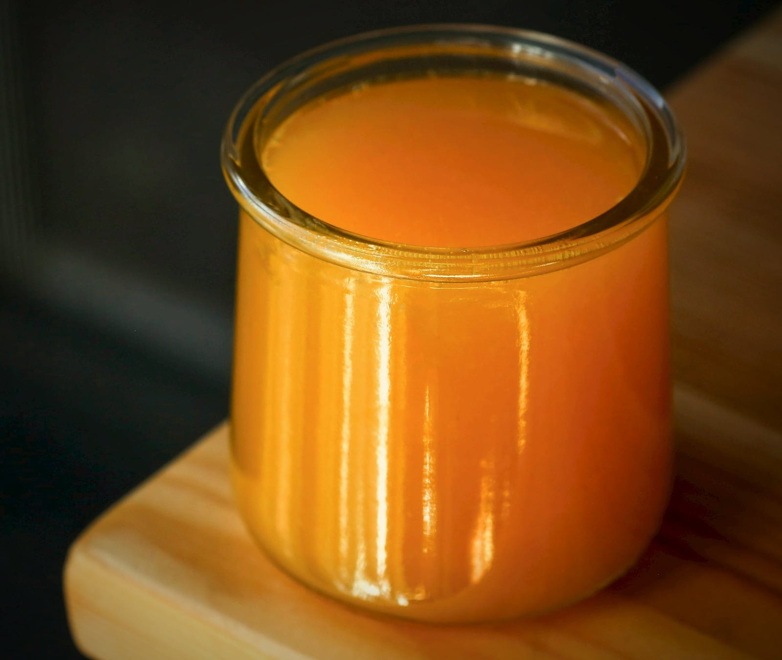 A glass jar of golden ghee on a wooden board