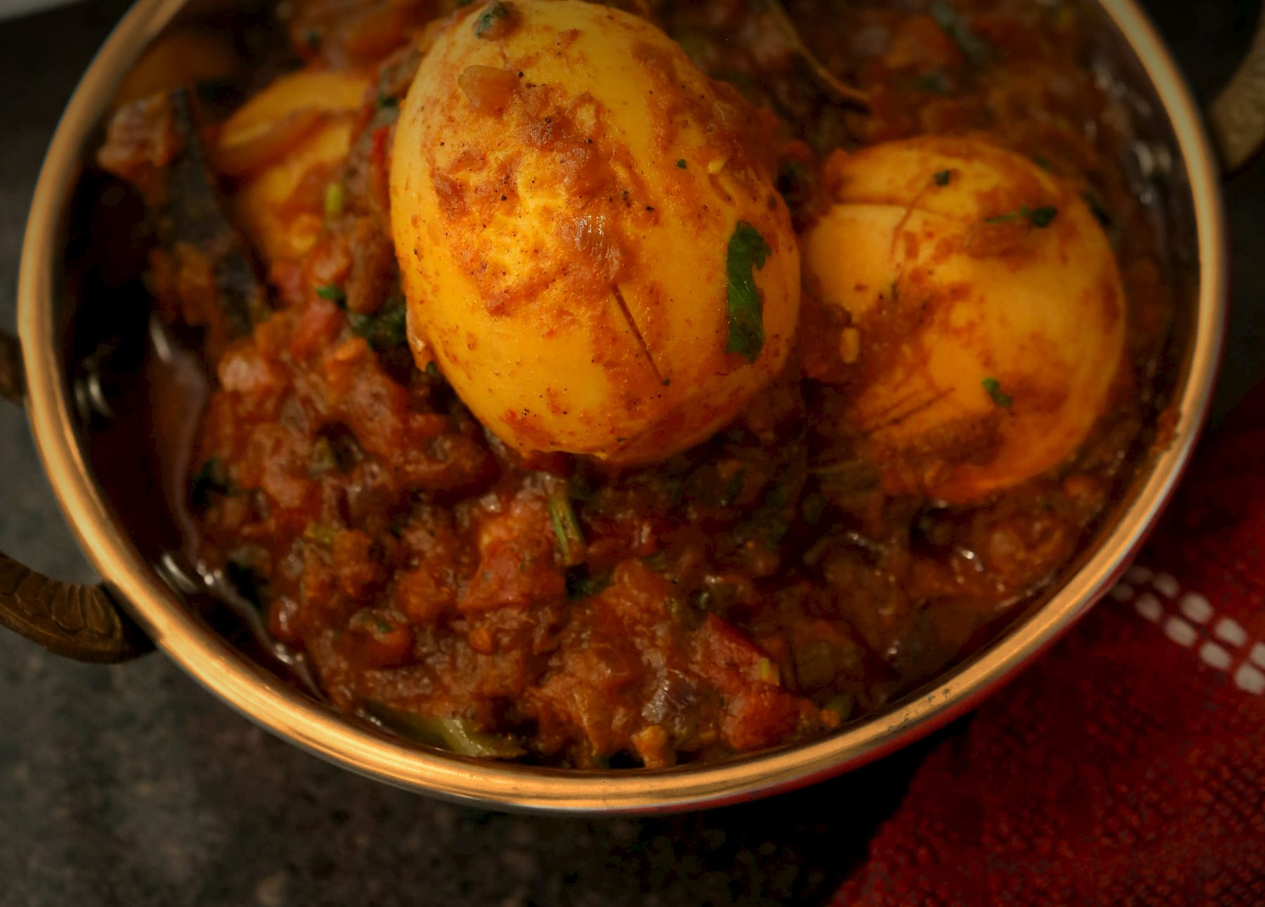 Three scored boiled eggs in a deep onion and tomato masala, in a polished brass kadai