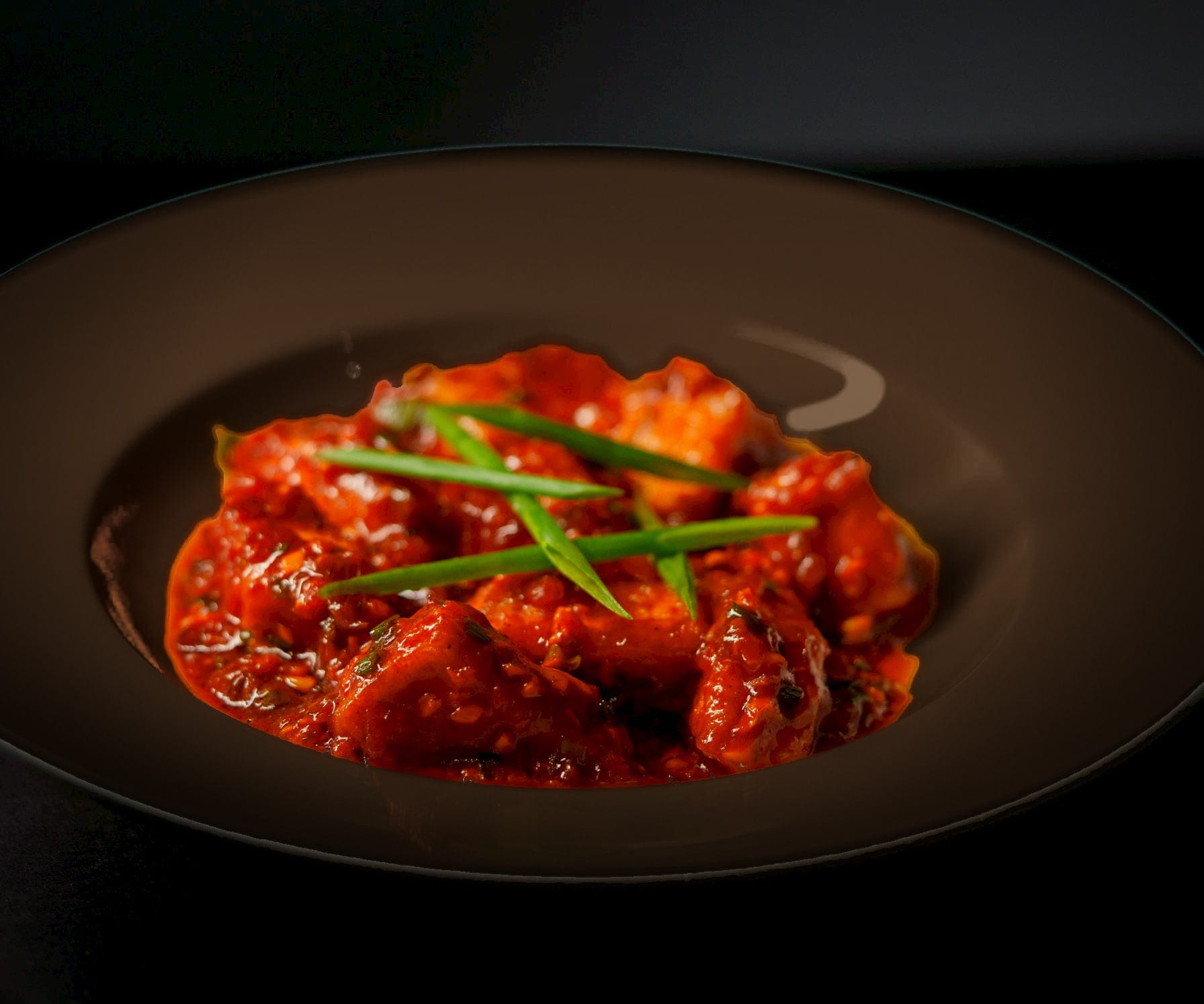 Paneer in a deep roasted red, semi-dry masala glossy with ghee, in a dark espresso stoneware bowl