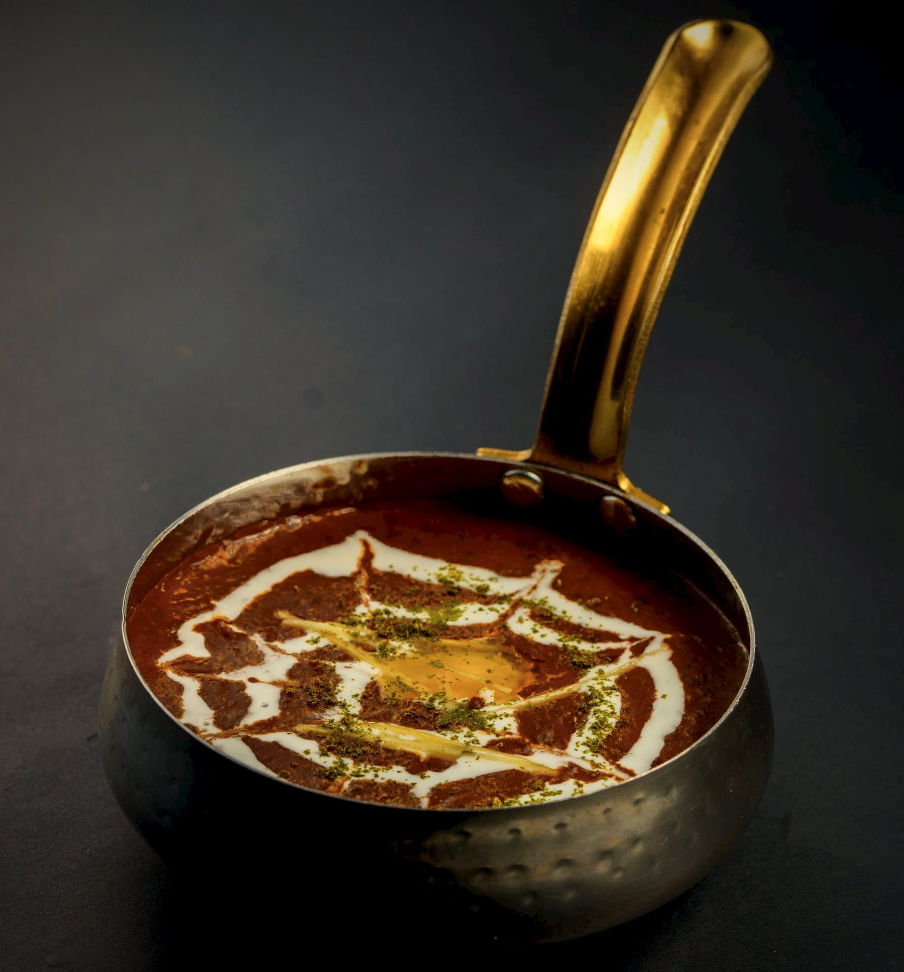 Glossy black dal with a web of cream, in a hammered handi with a brass handle